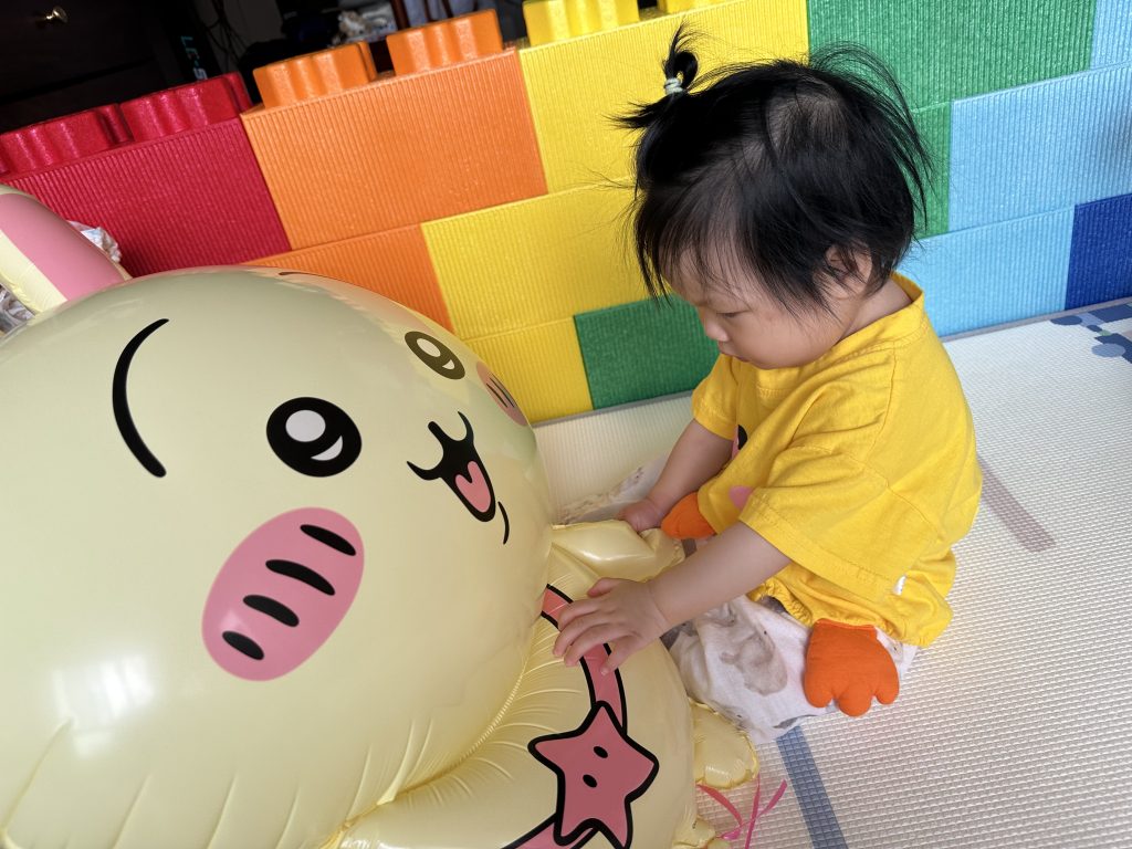 The baby is playing with cartoon balloons in a colorful foam playpen.