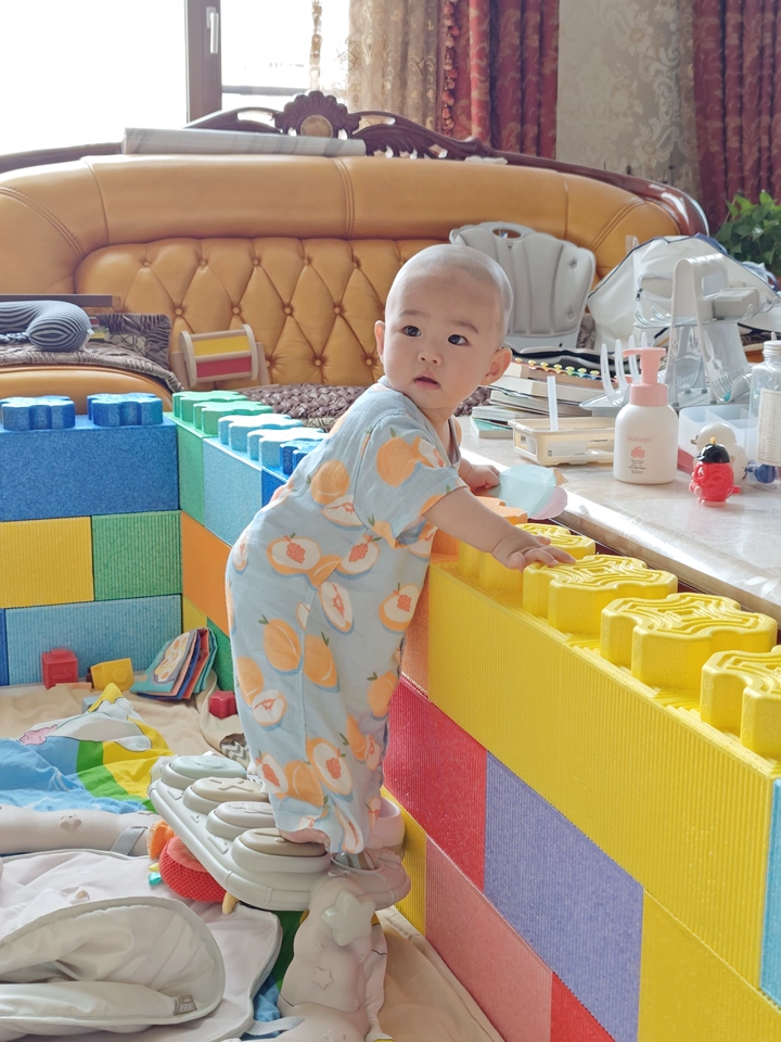 The baby is learning to walk while holding onto the fence.