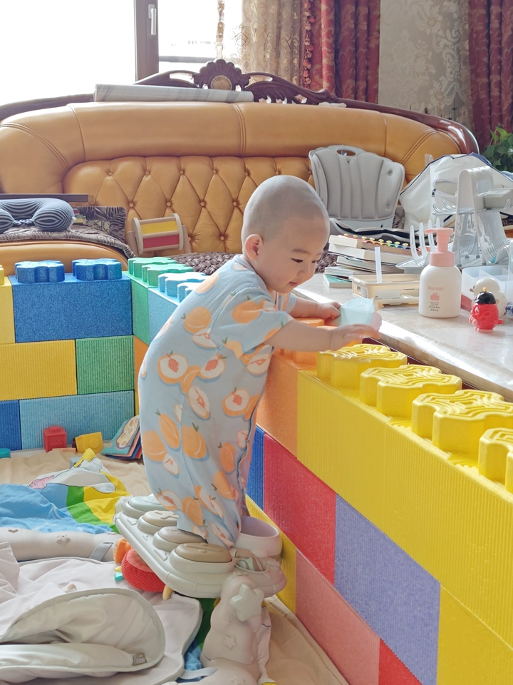 The baby is learning to walk while holding onto the fence.