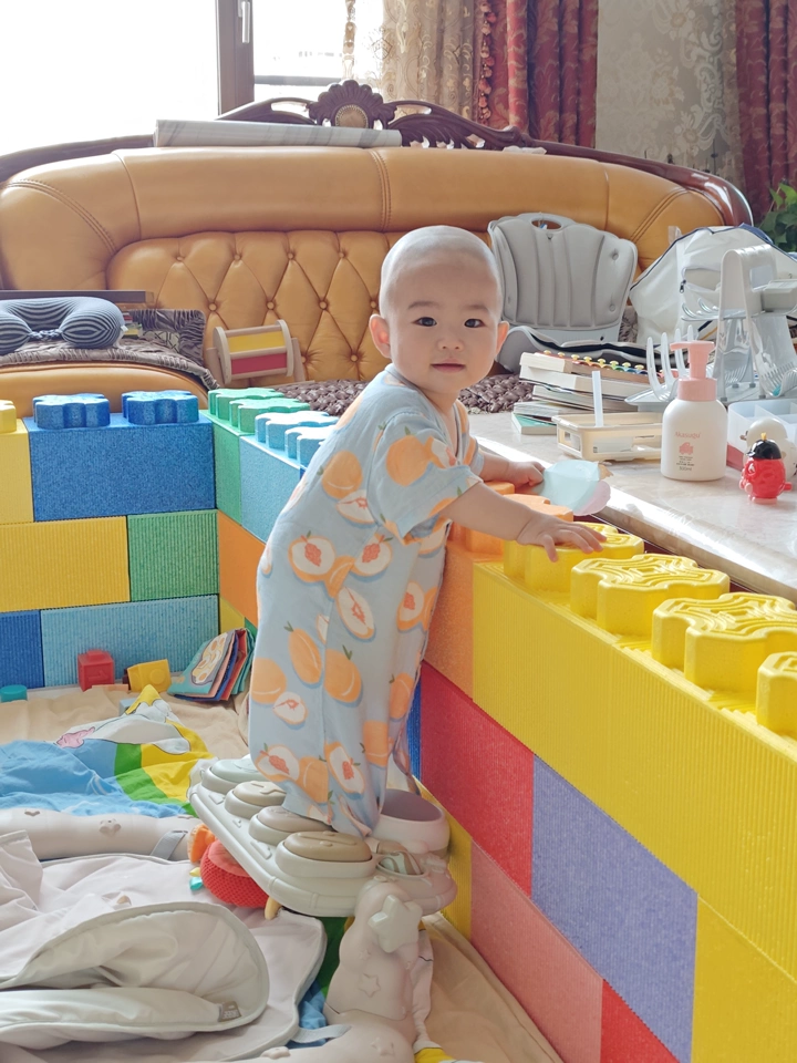 The baby stands holding onto the fence.